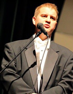 Man in suit speaking into a microphone at an event.