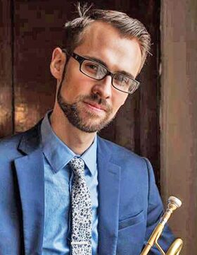 A man in glasses and a blue suit holding a trumpet.