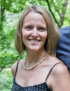 Smiling woman outdoors with short blonde hair and a beaded necklace.