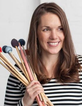 Woman smiling while holding makeup brushes.