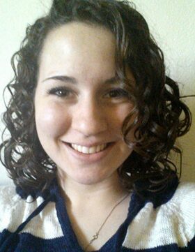 Smiling woman with curly hair wearing a white top.
