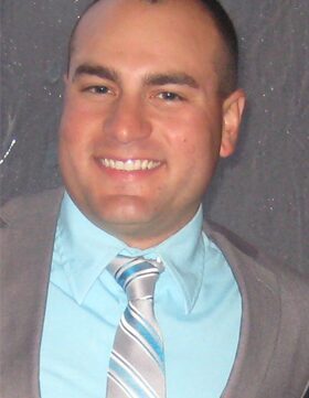 Smiling man dressed in a light blue shirt and striped tie.