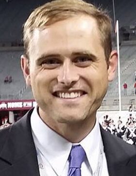 Smiling man in a suit at a stadium event.