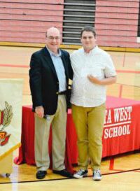 Two men posing in a school gym with a red tablecloth.