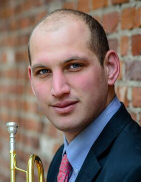 Portrait of a man in a suit holding a trumpet against a brick wall.