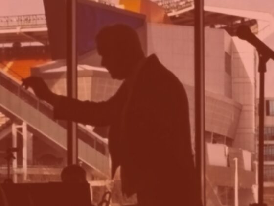 Silhouette of a man speaking indoors with a large window background.