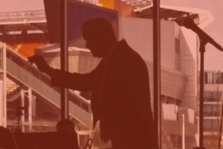 Silhouette of a man speaking indoors with a large window background.