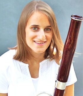 Young woman holding a bassoon and smiling.
