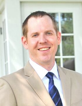 Man in beige suit smiling indoors.