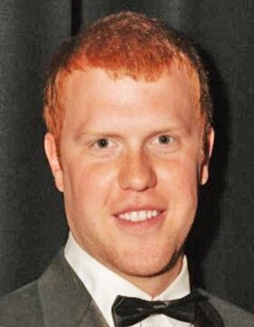 A smiling man with red hair in formal attire.